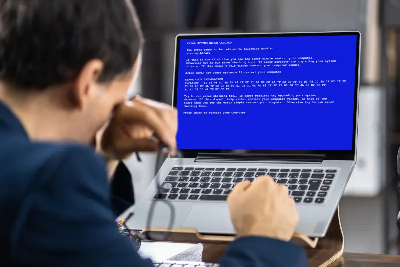 A businessman stares at the Blue Screen of Death on his laptop.